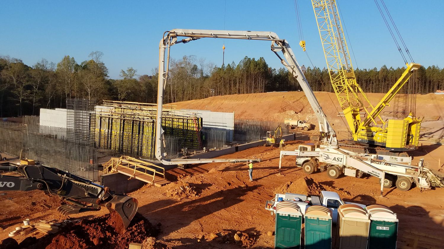 Concrete boom pump reaching over rebar and formwork with a crane standing by.