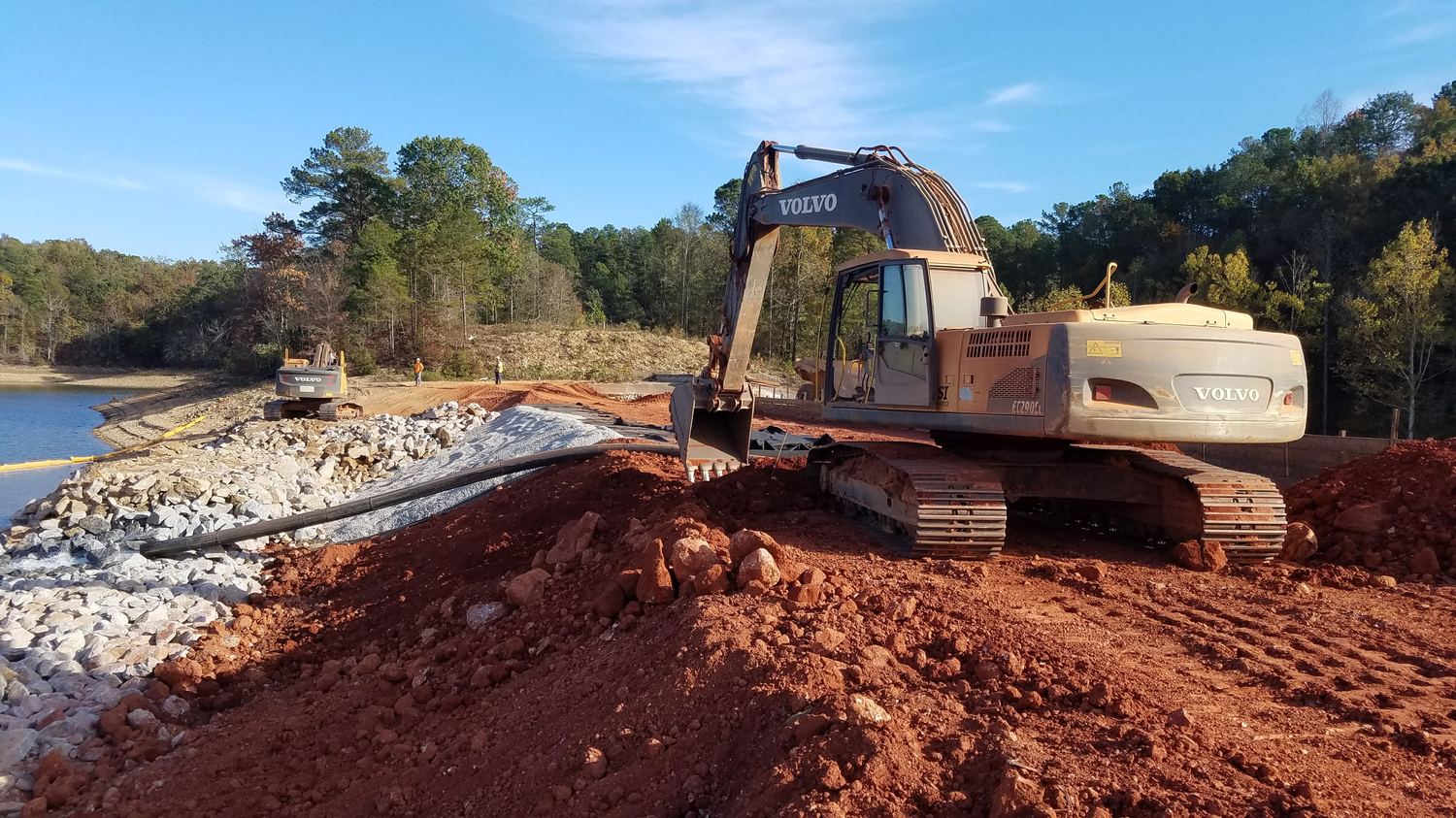 Excavator placing armor stone over bedding and geotextile at the shoreline.