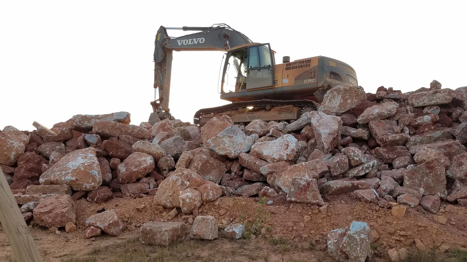 Excavator perched atop a stockpile of broken stone.