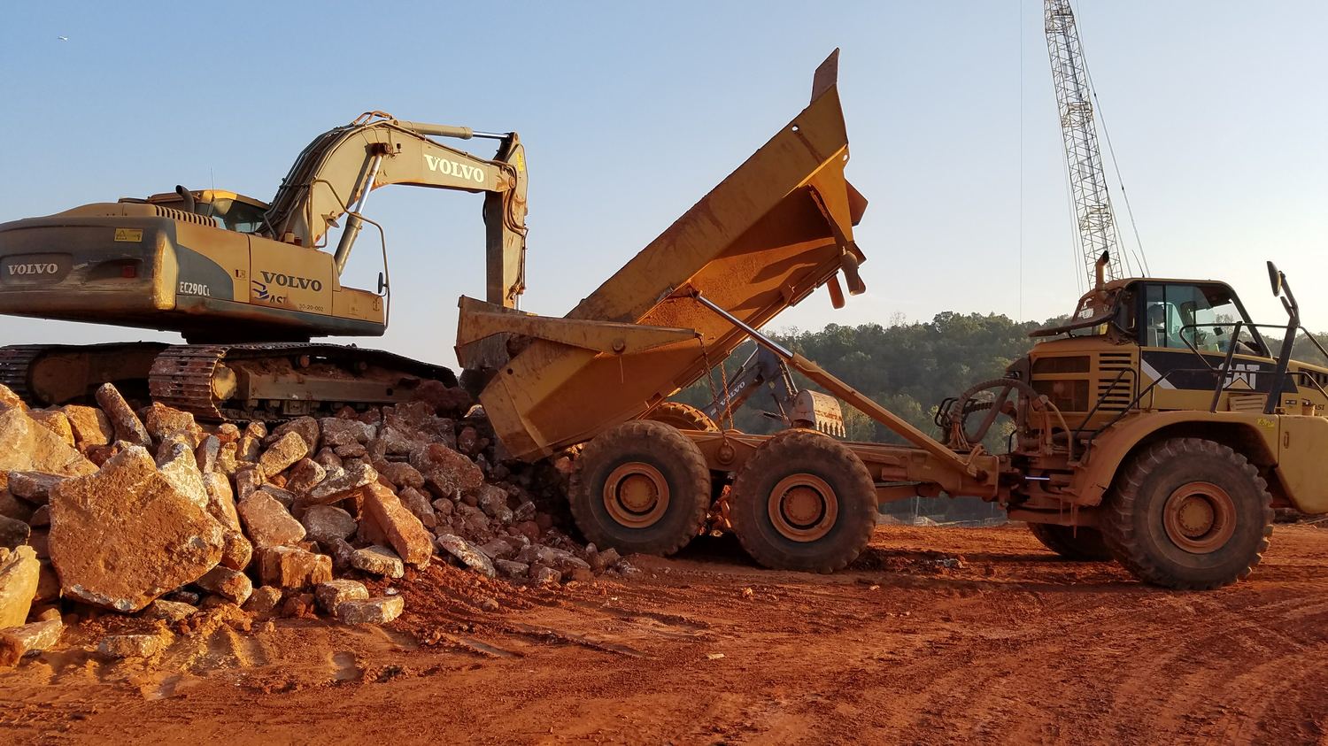Excavator loading an articulated rock truck with a crane tower behind.