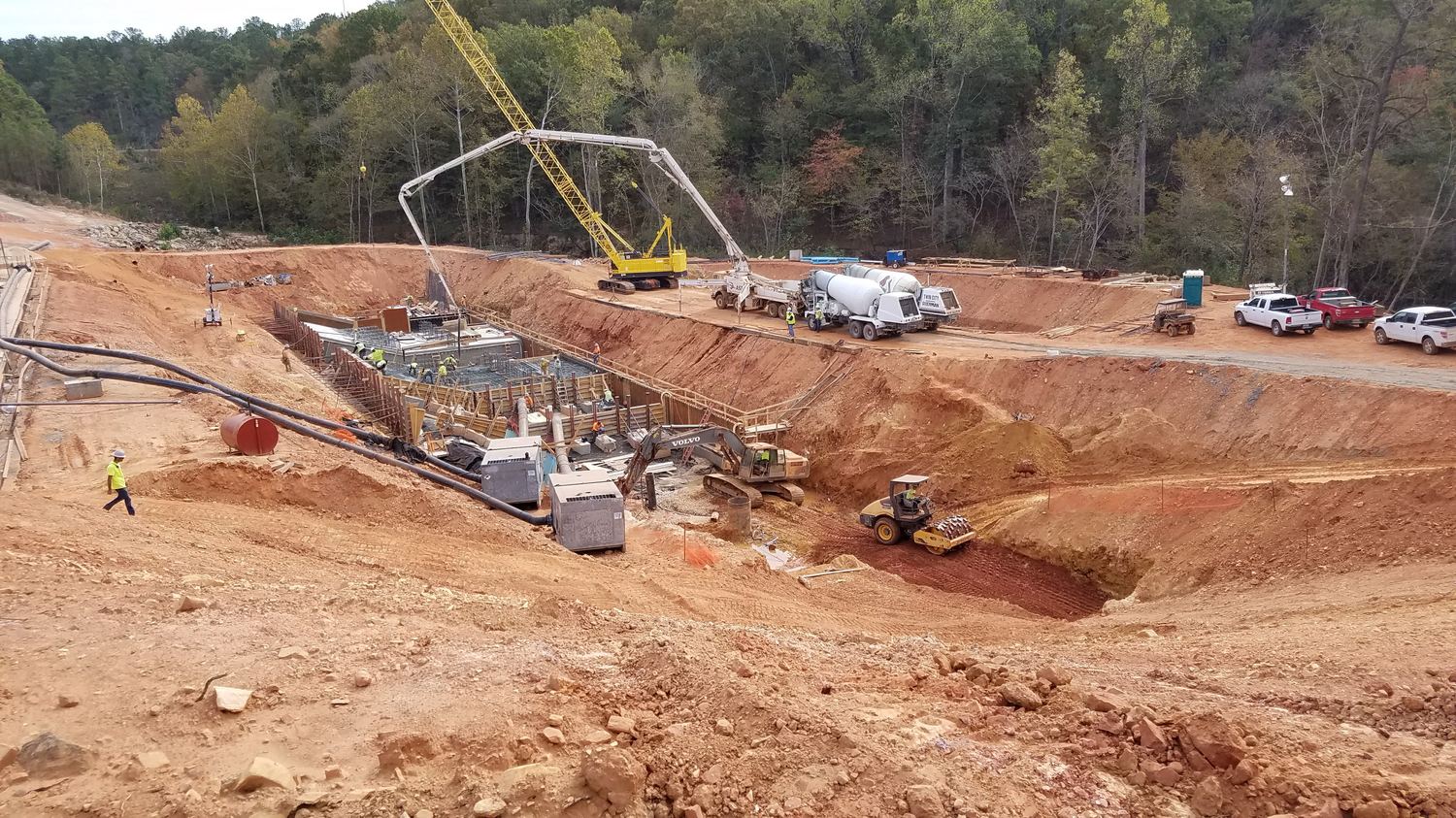 Wide view of a structure excavation with concrete pump truck, crane, and crew.