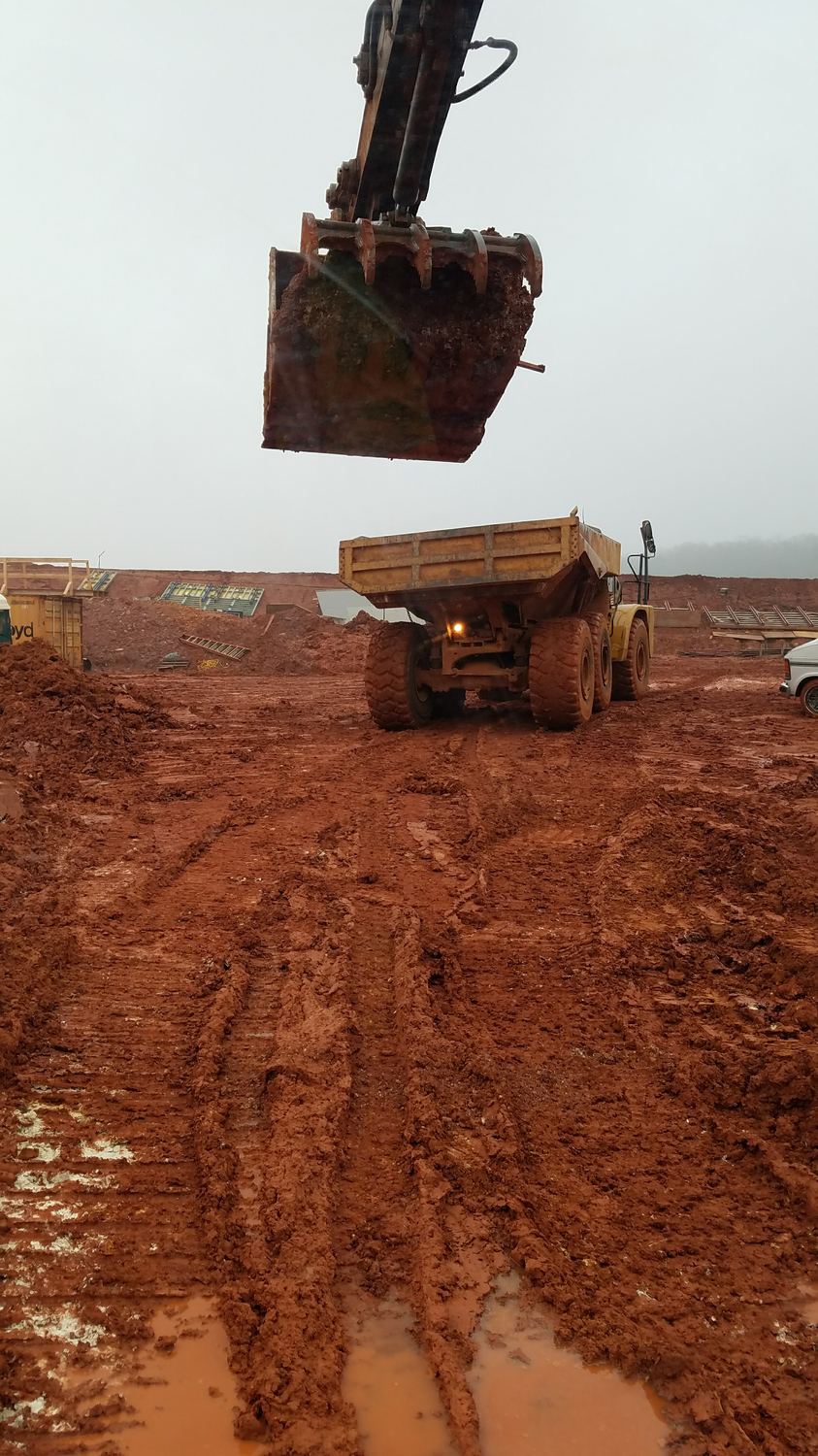 Excavator bucket swinging a load into a haul truck in the rain.