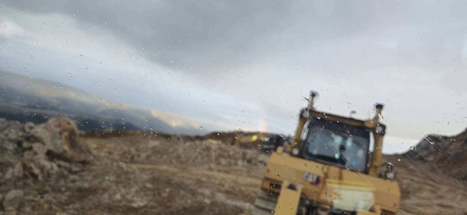 Rain-streaked windshield with a dozer visible ahead on the cut.