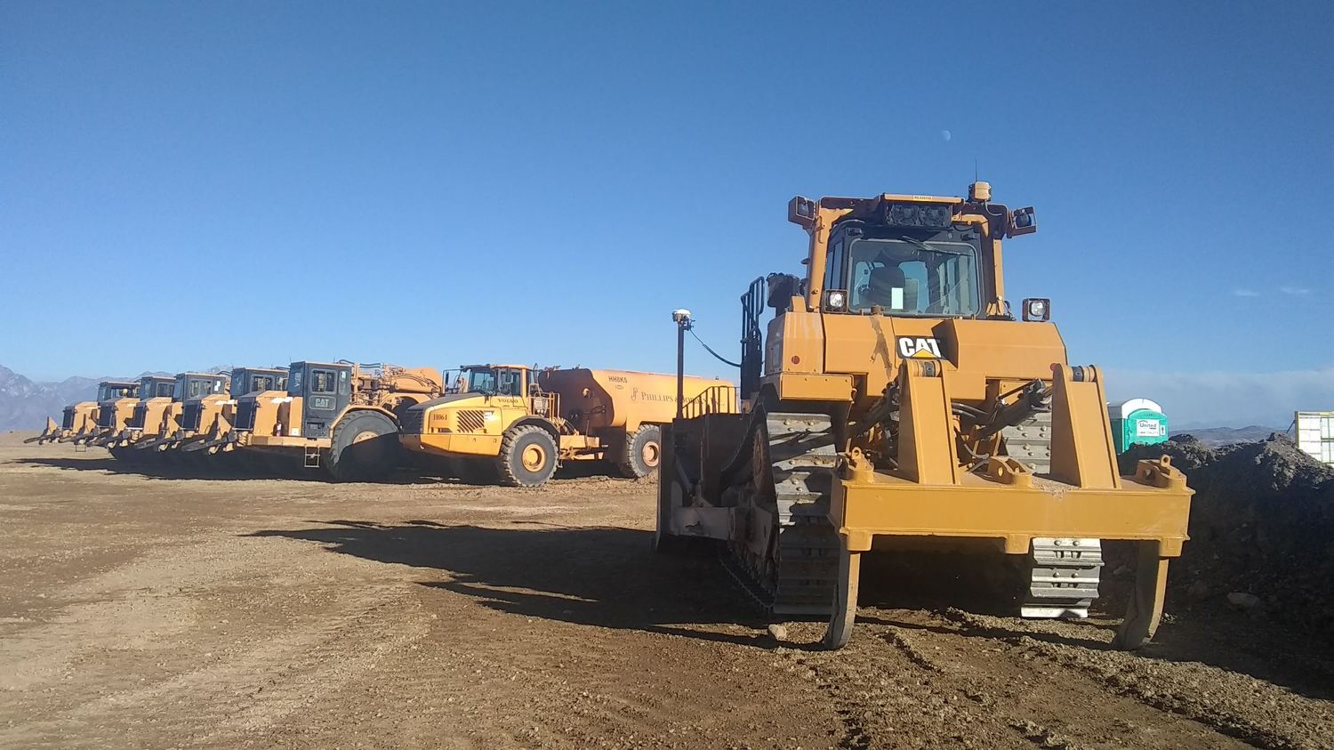 Dozer in front of a scraper train and water truck staged behind.