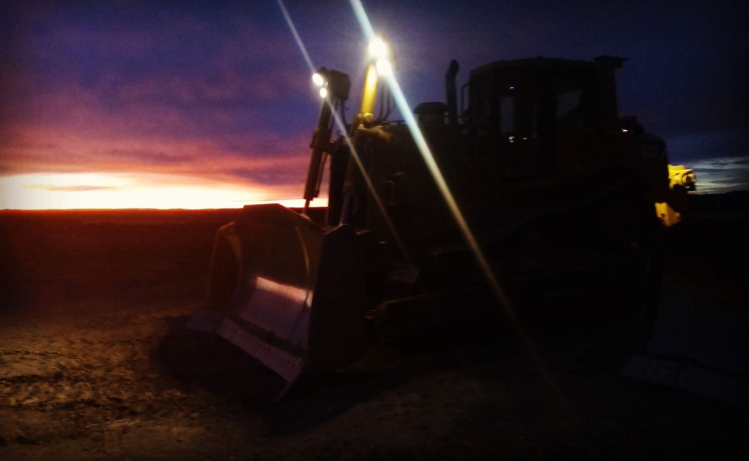 Dozer bucket in silhouette against a burning sunset sky.
