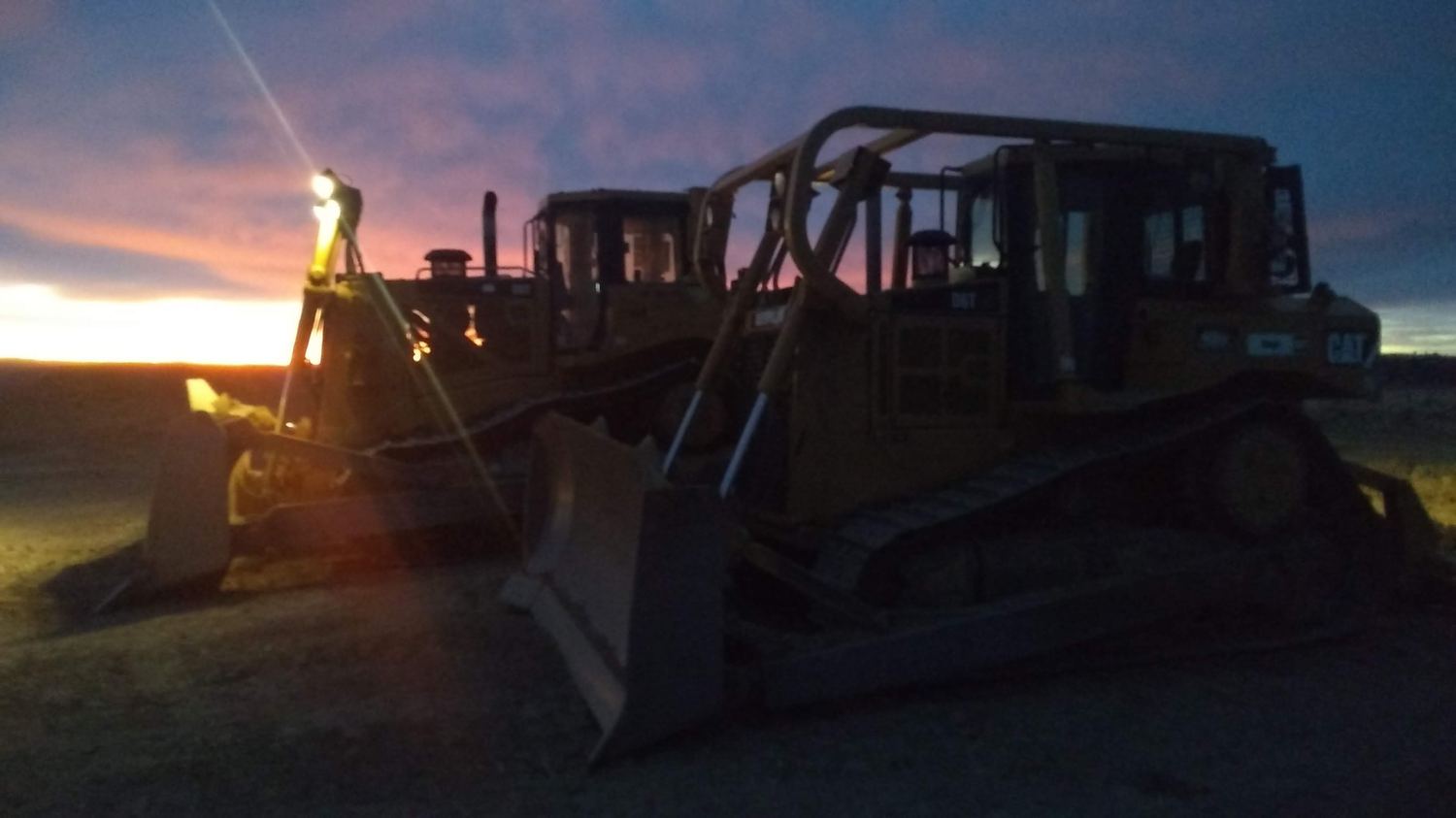 Two dozers silhouetted against pink and blue evening light.