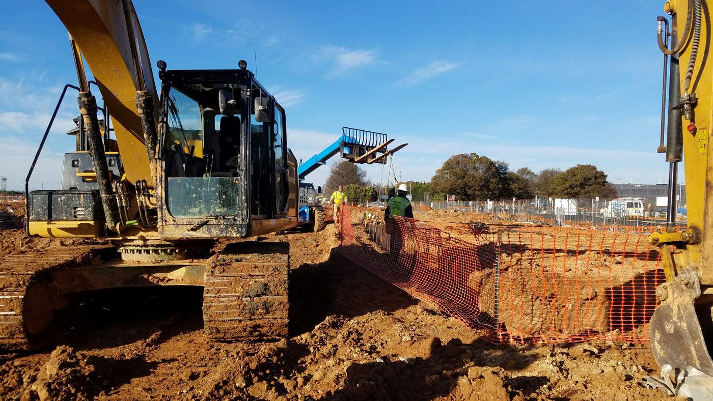 Excavator and telehandler working with crew and safety fencing on an airport expansion site.