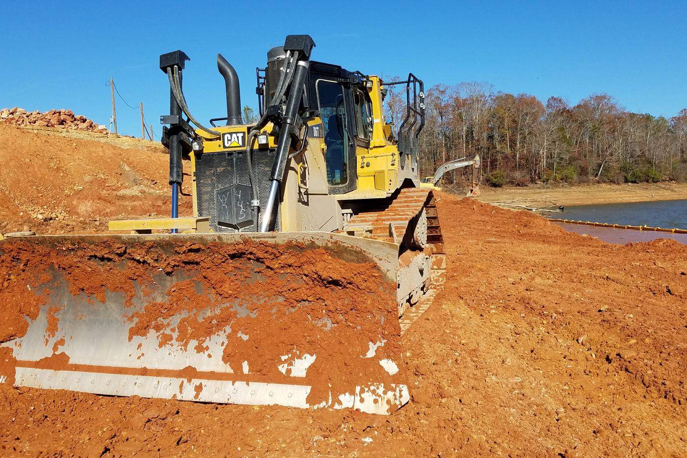 Cat D6T dozer with a loaded blade of red clay on an embankment.