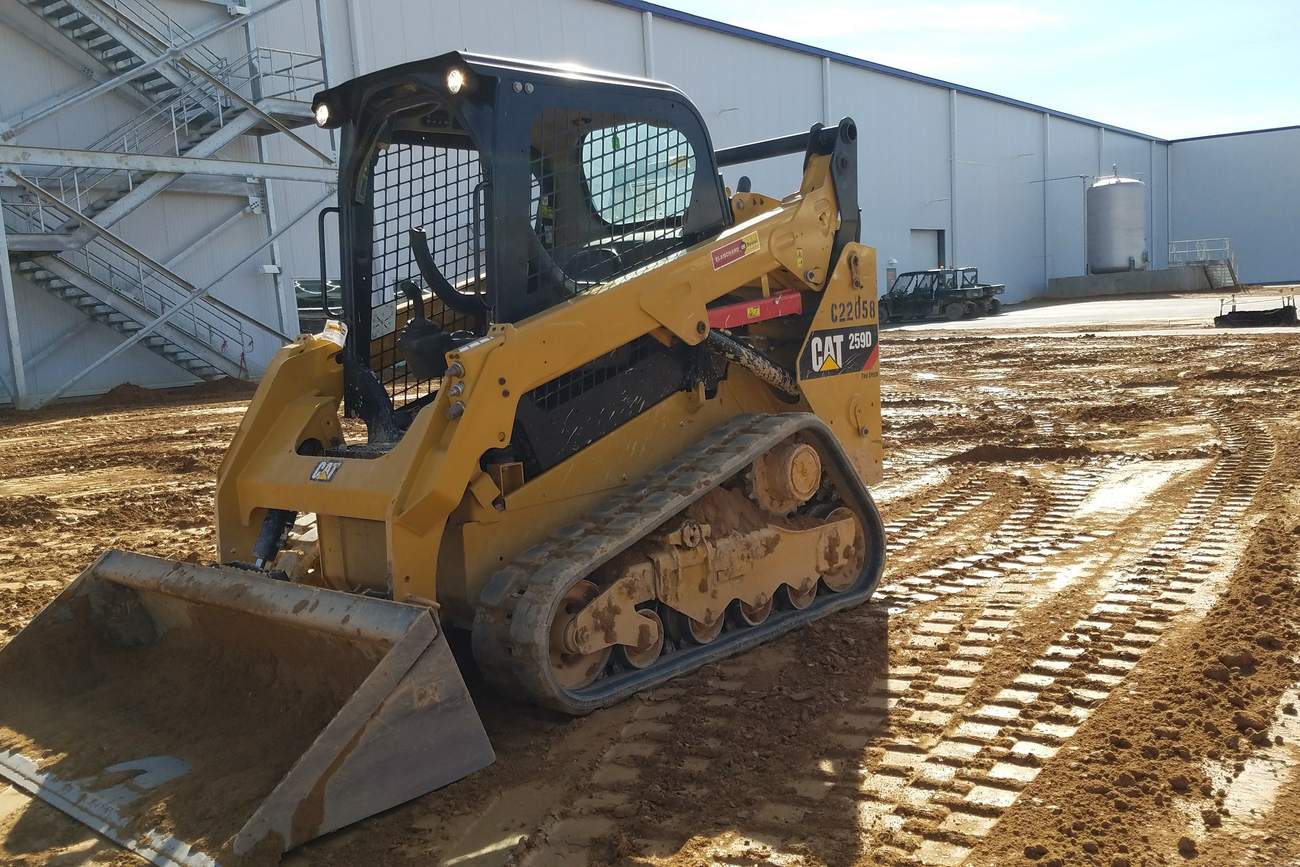 Cat 259D compact track loader grading beside an industrial building.