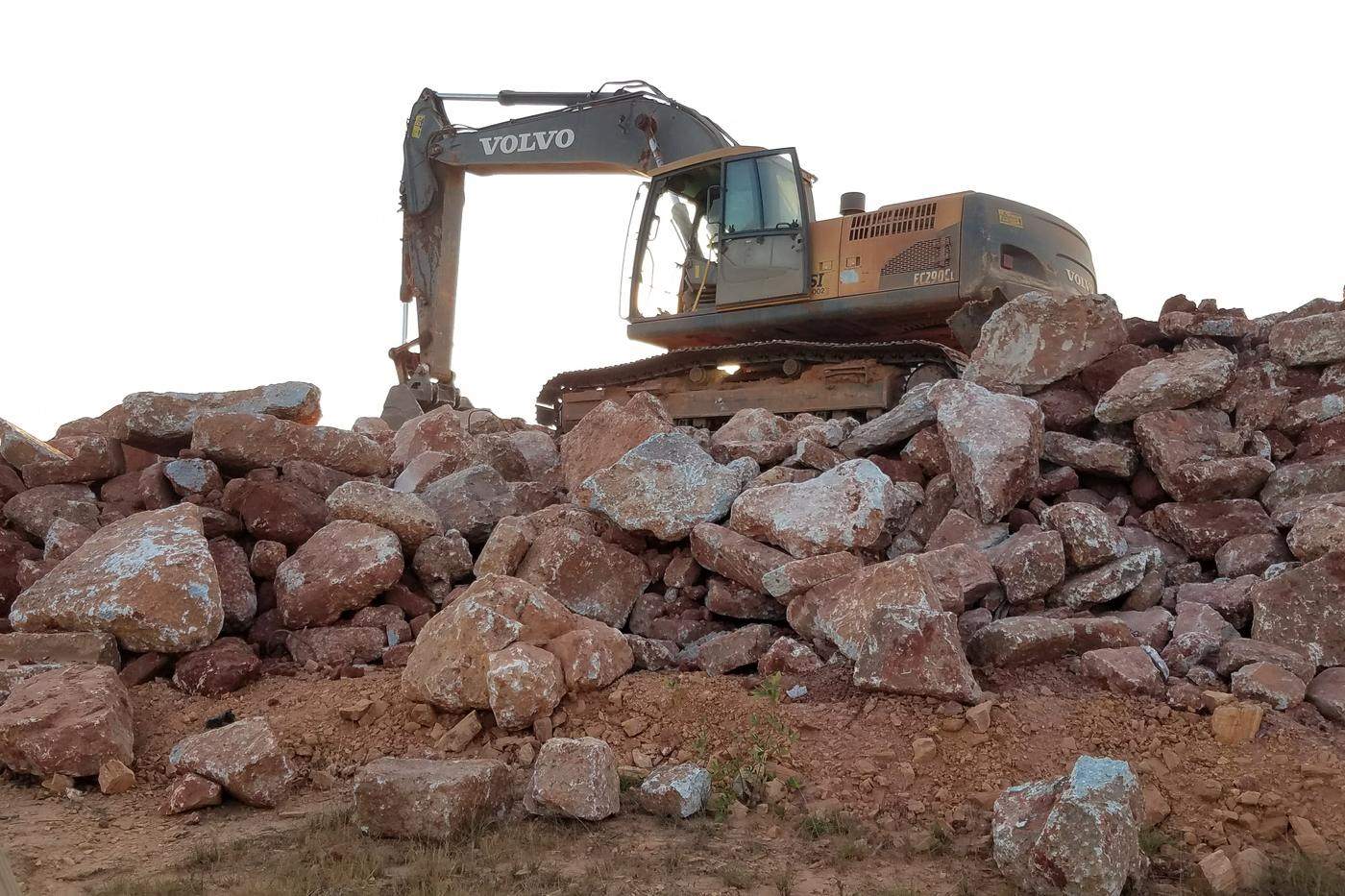 Excavators placing armor stone over bedding along a reservoir slope.