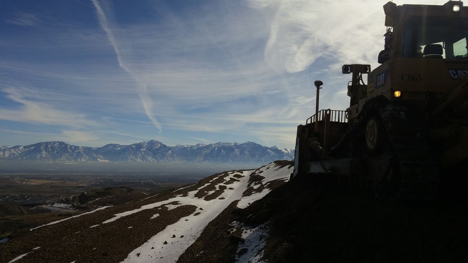 Dozer silhouette on a ridge above a hazy valley.