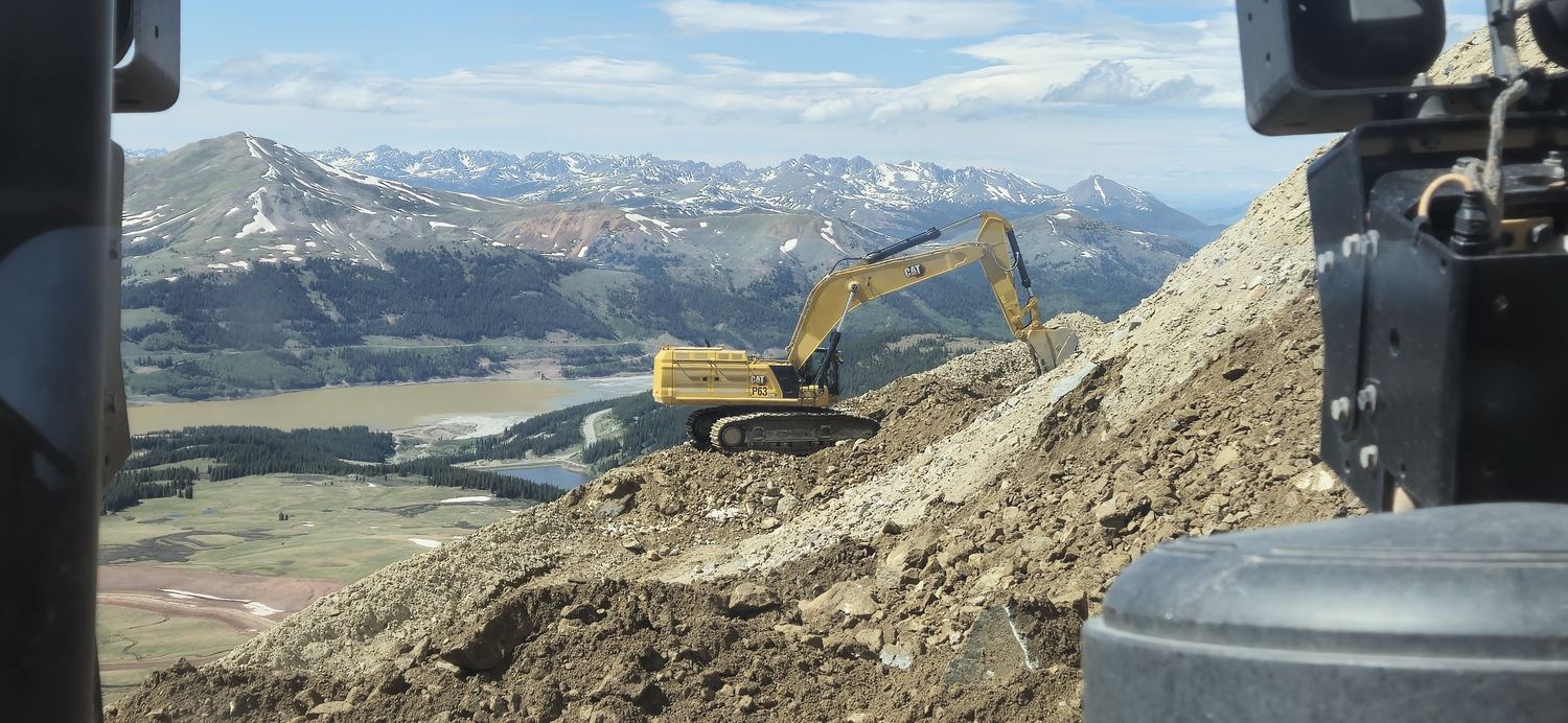 Excavator working a rock ridge above an alpine lake.