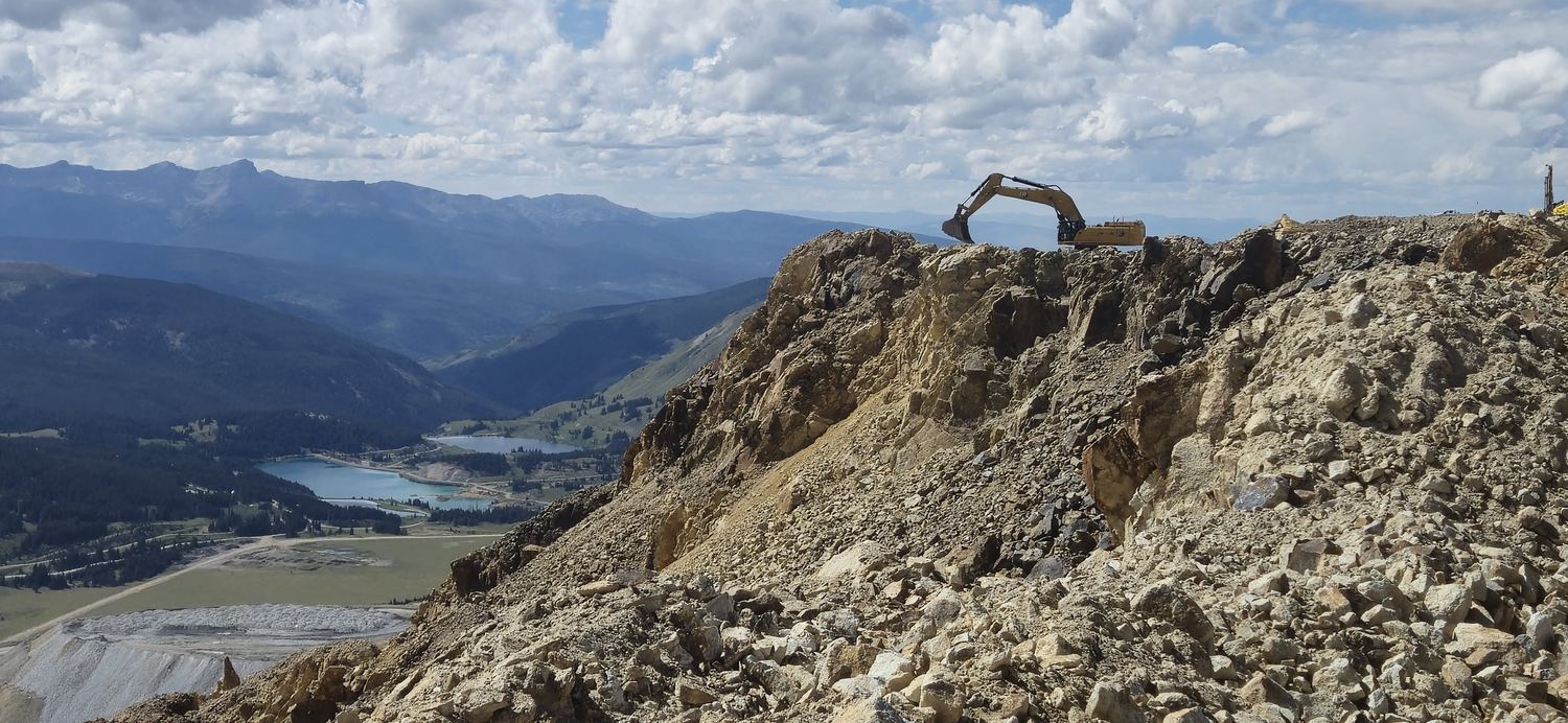 Excavator working a rock ridge above two alpine lakes.