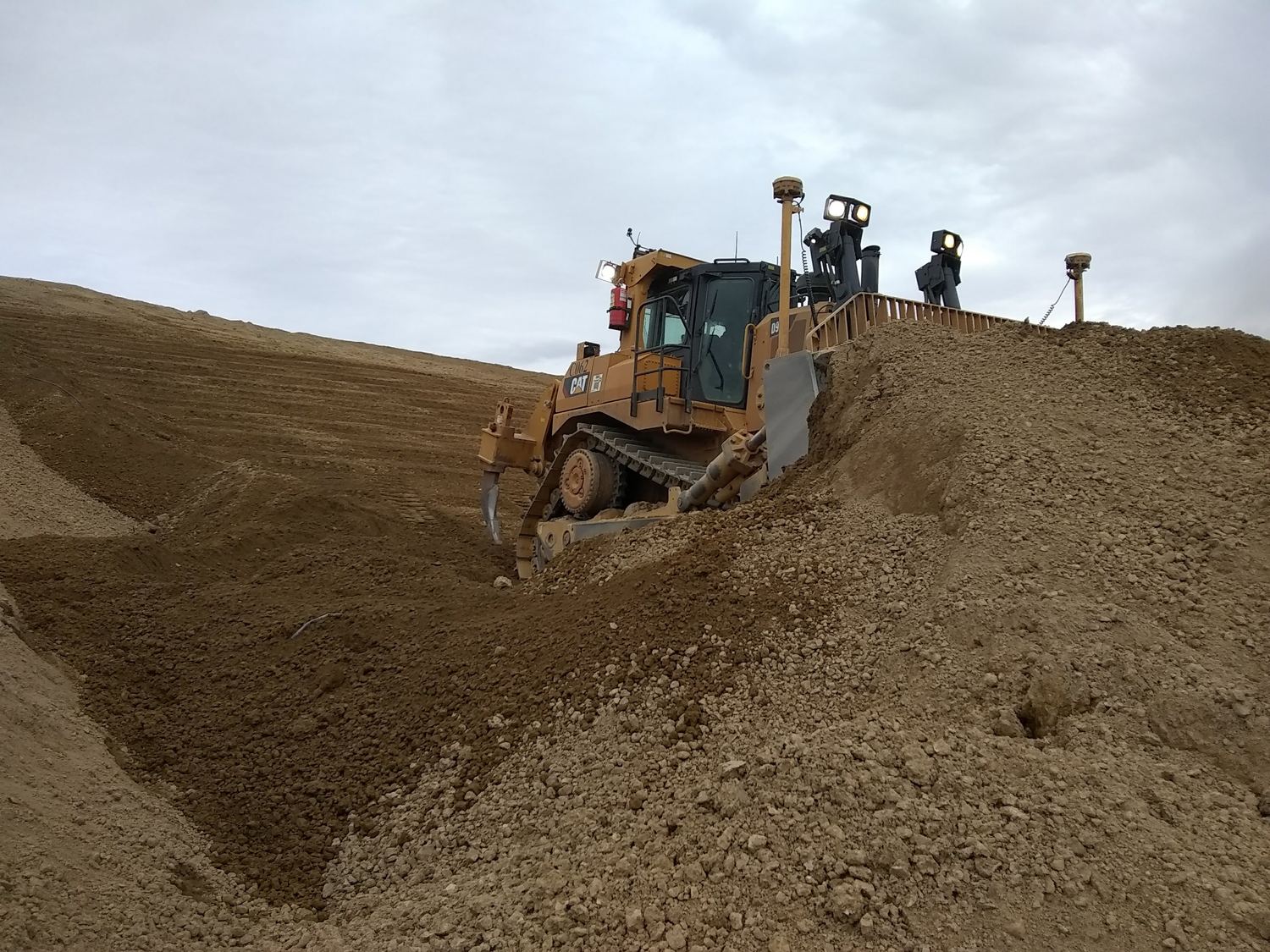 CAT D9 dozer cresting a stockpile with light towers.