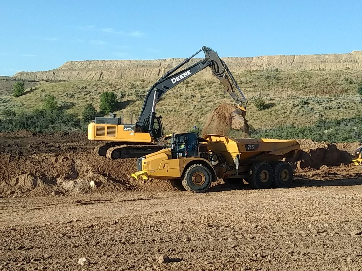 John Deere excavator loading a CAT articulated truck during reclamation grading.