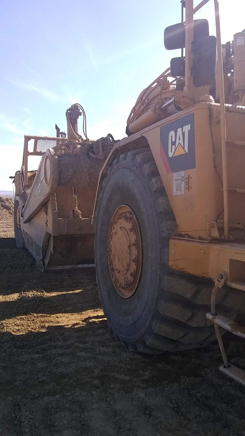 CAT wheel tractor-scraper loaded and moving, tire in foreground.