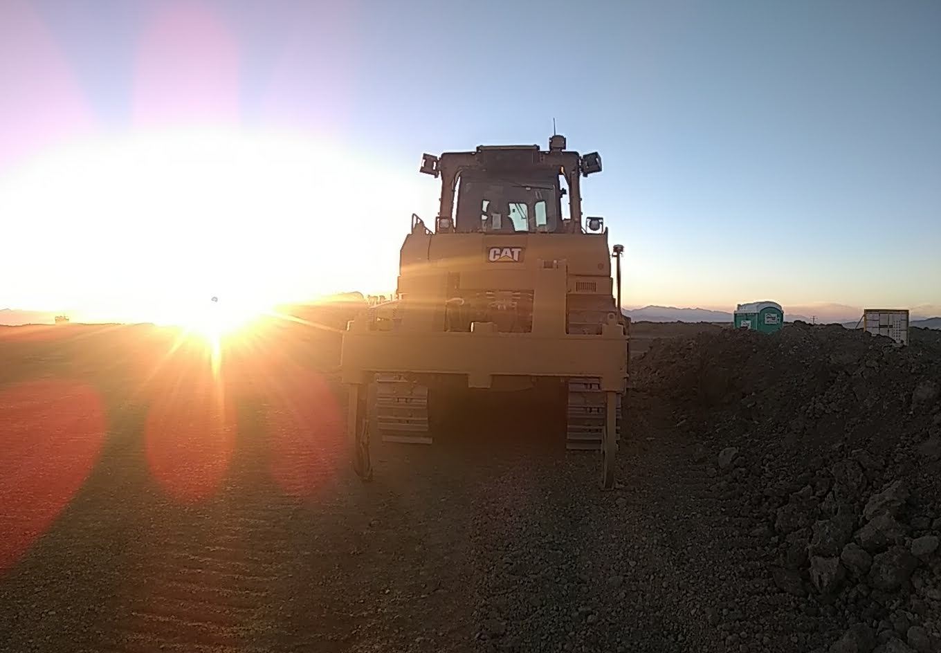 Dozer backlit at sunrise beside a stockpile.