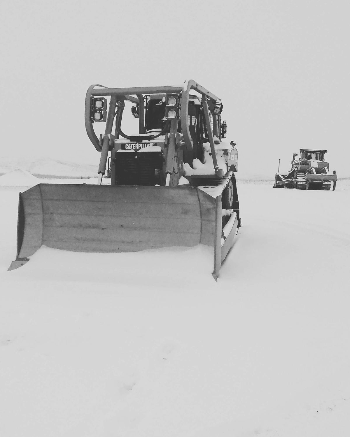 Two dozers parked on a snow-covered pad in winter.