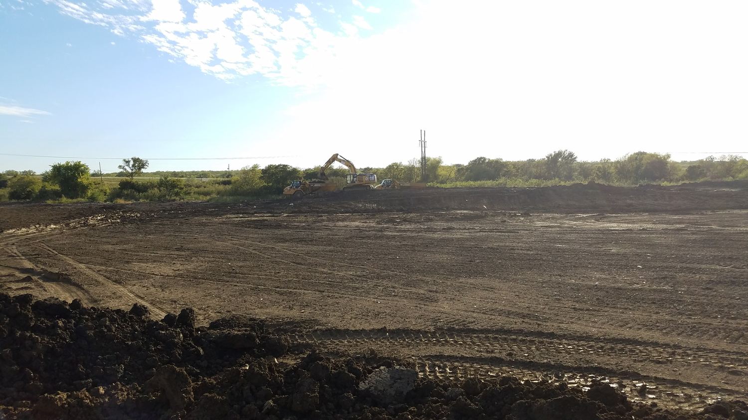 Excavator loading haul trucks at the edge of a cleared area.