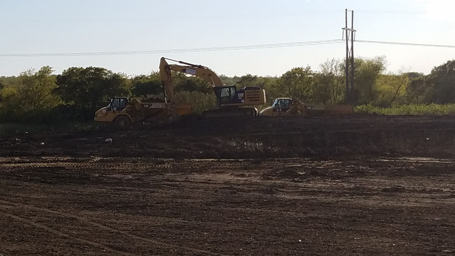 Excavator and articulated trucks working the cut near a power line.