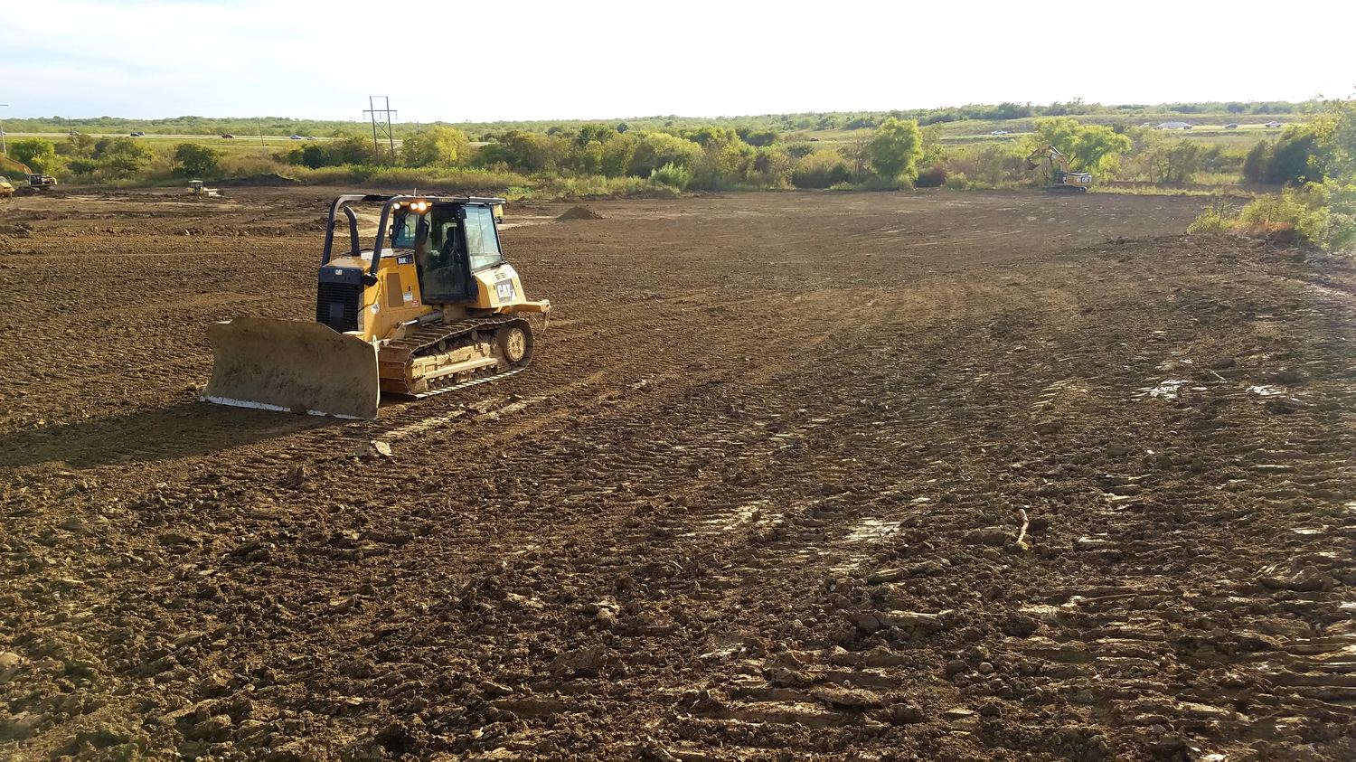 Dozer working a large graded pad with more equipment active in the distance.