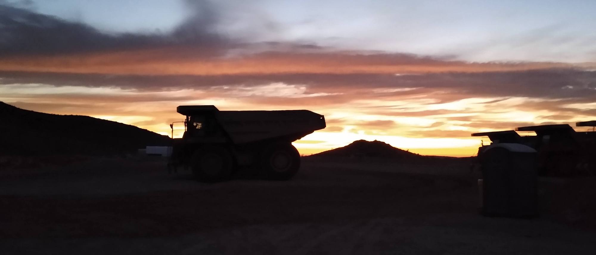Haul truck silhouetted against a desert sunrise on a mine site.