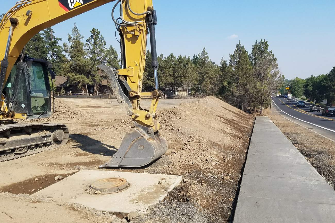 Cat excavator on a cut slope above a new sidewalk in central Oregon.
