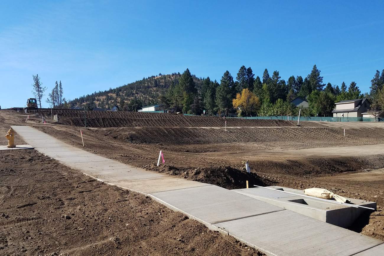 Excavator working alongside a new sidewalk and manhole on a central Oregon road.