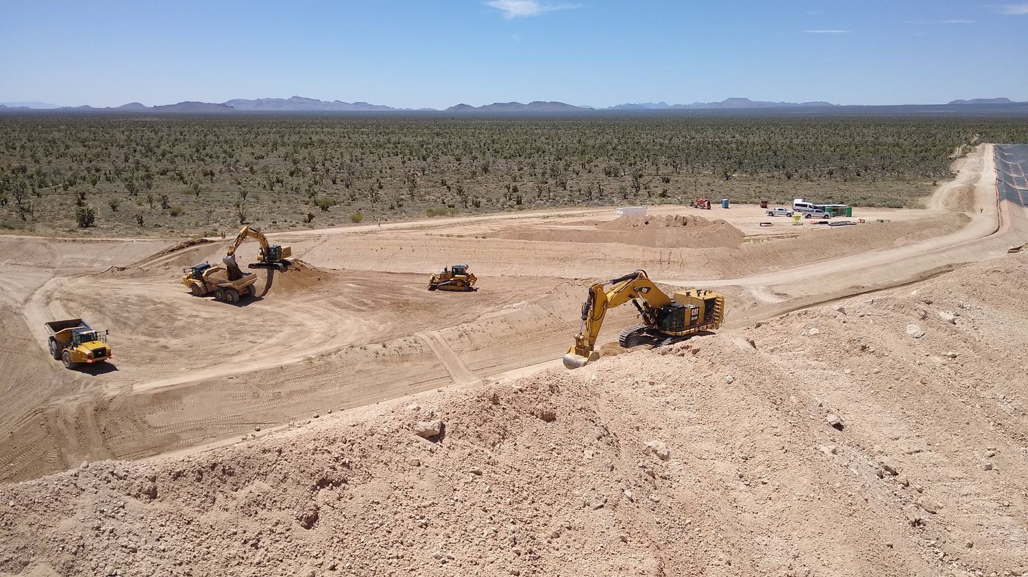 Motor grader working a haul road with an empty scraper pan staged behind.