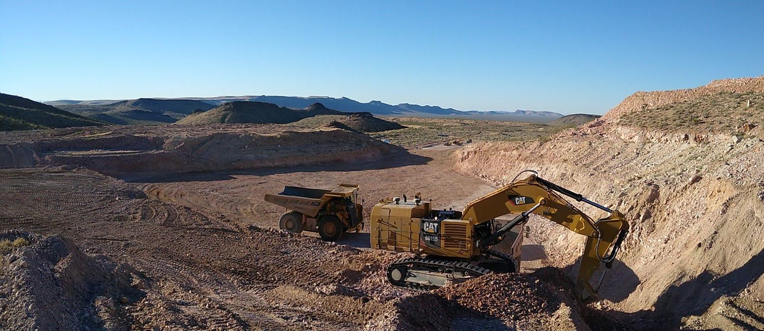 Excavators, dozer, and haul trucks working a wide bench in the desert.