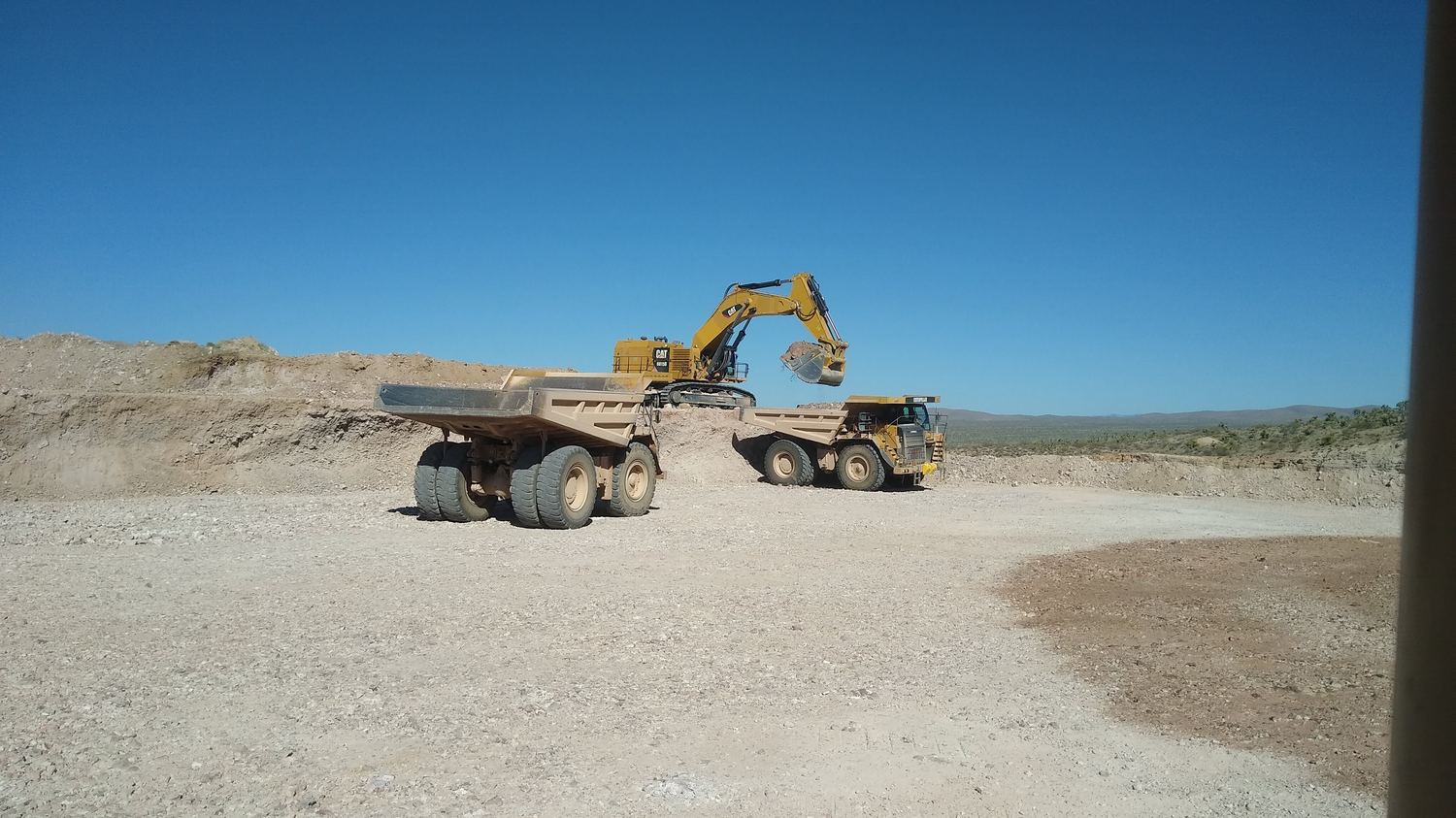 Excavator loading a rigid-frame haul truck at the pit floor.