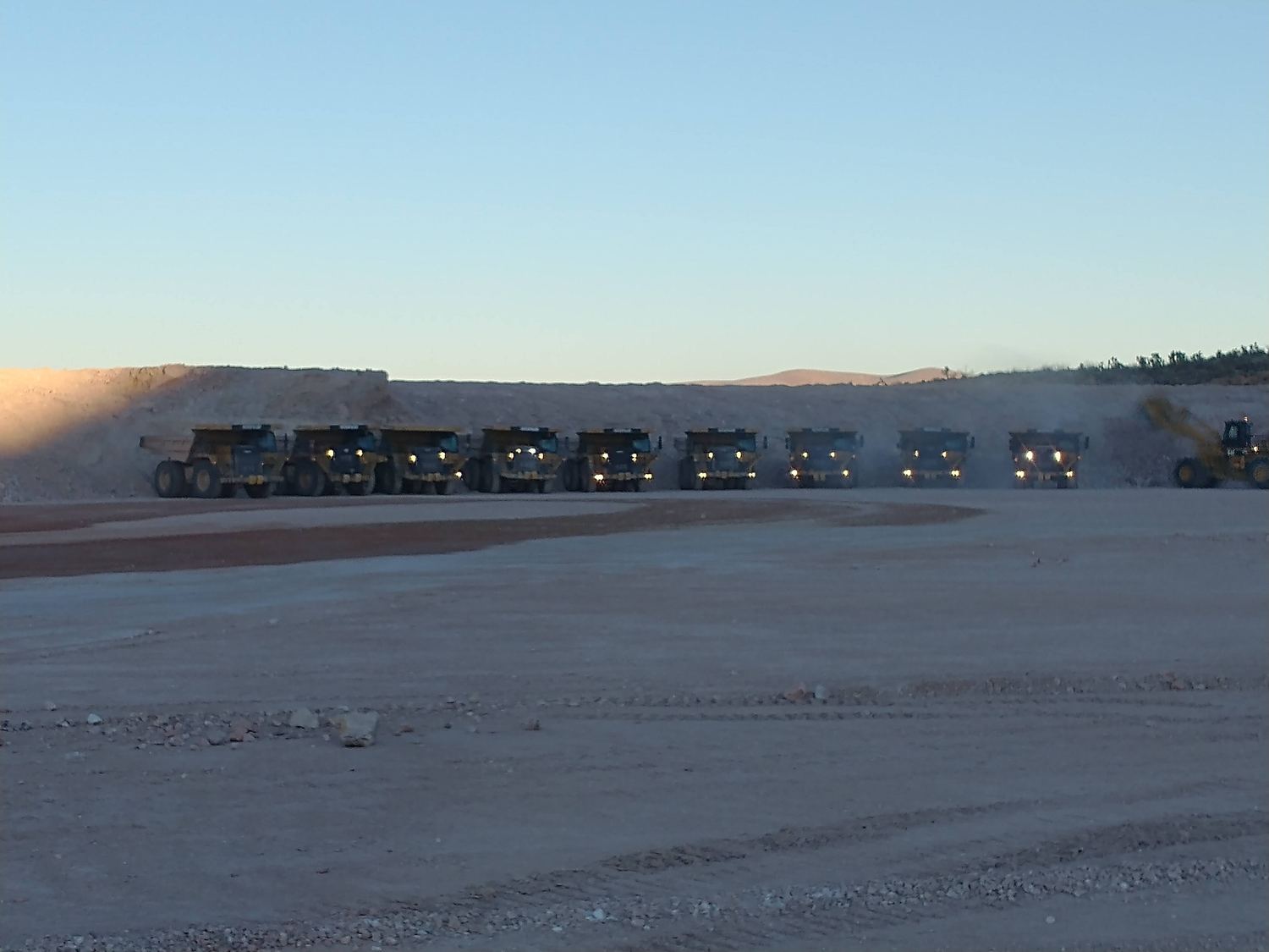 Rigid-frame haul truck crossing open pit floor, dust trailing behind.